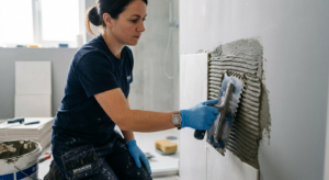 A close-up, professional photograph of a tiler using a notched trowel to apply adhesive mortar onto